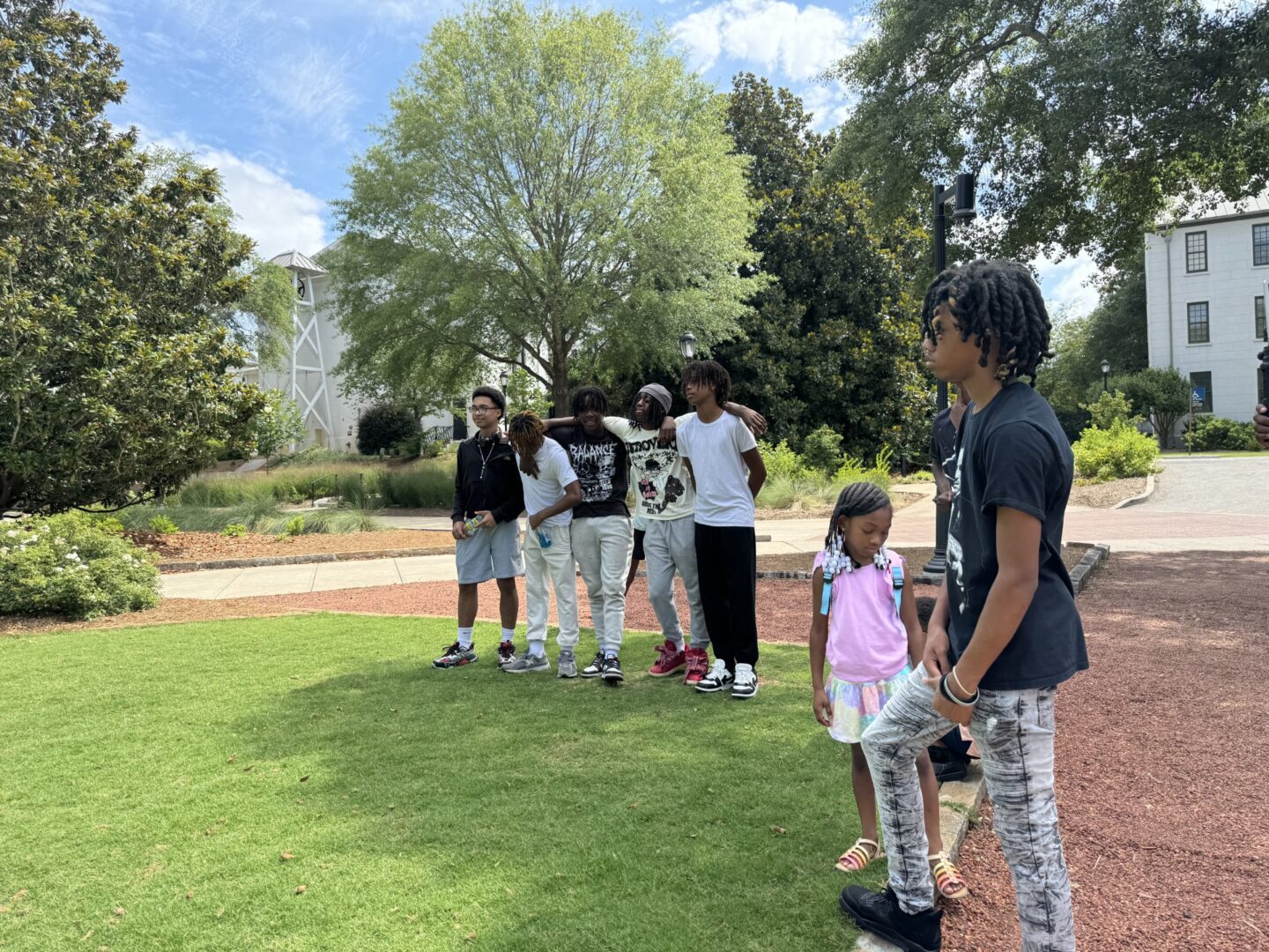 Group of people standing and interacting outdoors on a sunny day.