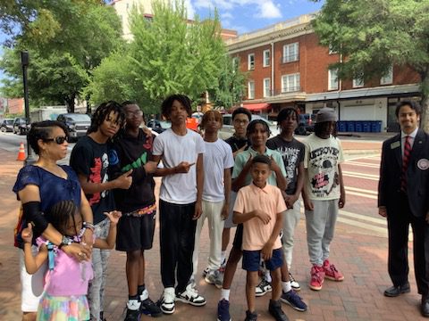 A group of diverse young people gathers outdoors on a sunny day.