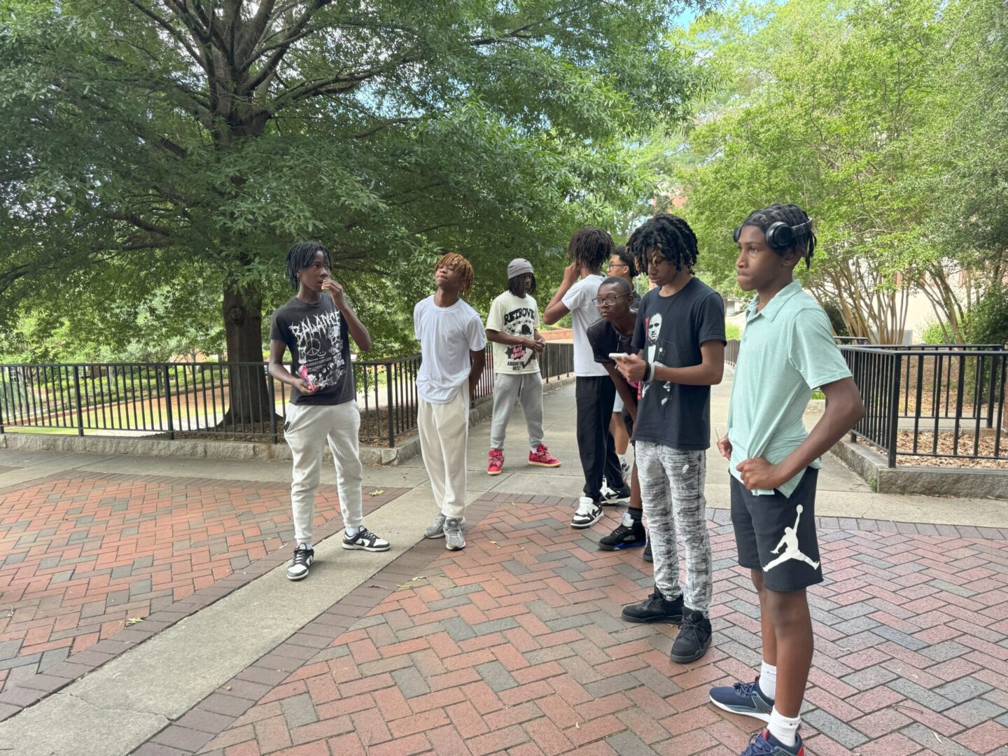 A group of six young men standing on a brick pathway near trees.