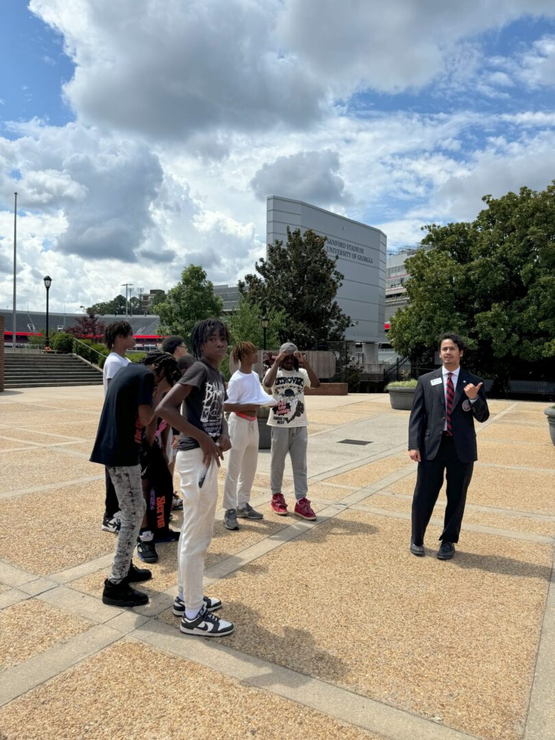 A group of people gathered outdoors, some engaged in conversation, under a partly cloudy sky.